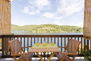 A wooden deck with two chairs and a table, overlooking a lake and hills. - Apartments Matana Chano (Mljet)