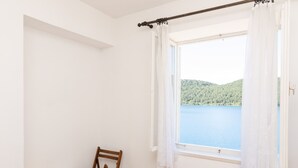 A room with a window overlooking a lake, a table with fruits, and a chair. - Apartments Palma (Mljet)