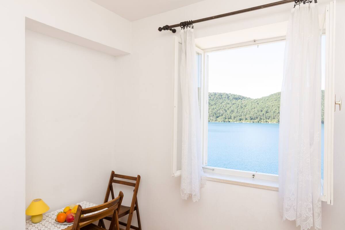 A room with a window overlooking a lake, a table with fruits, and a chair.