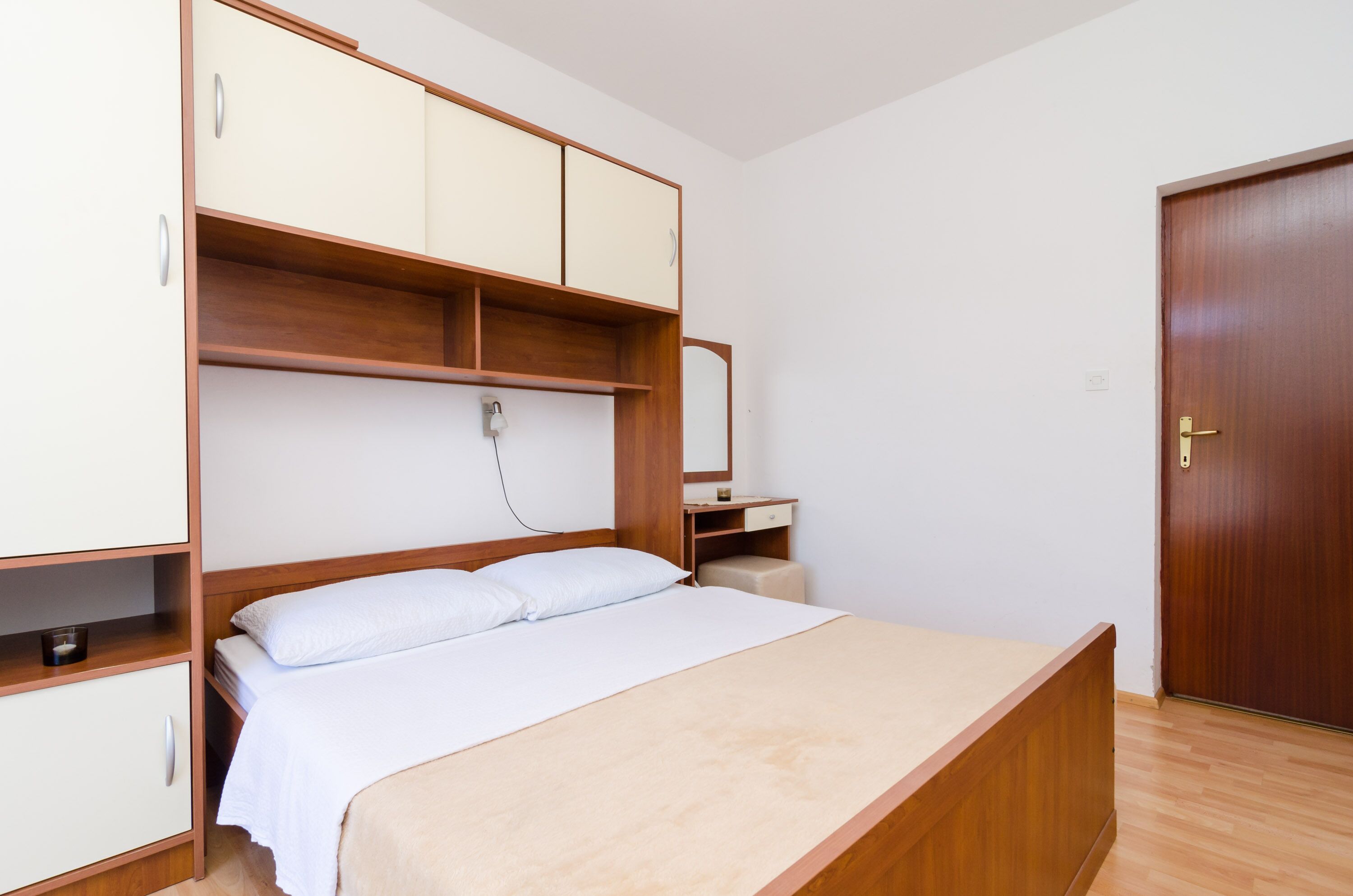 Een slaapkamer met een houten bed, een nachtkastje, een kledingkast en een deur.