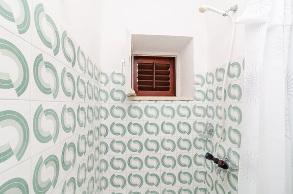 A bathroom with patterned tiles, a window with a wooden shutter, and a shower area. - Apartments Palma (Mljet)