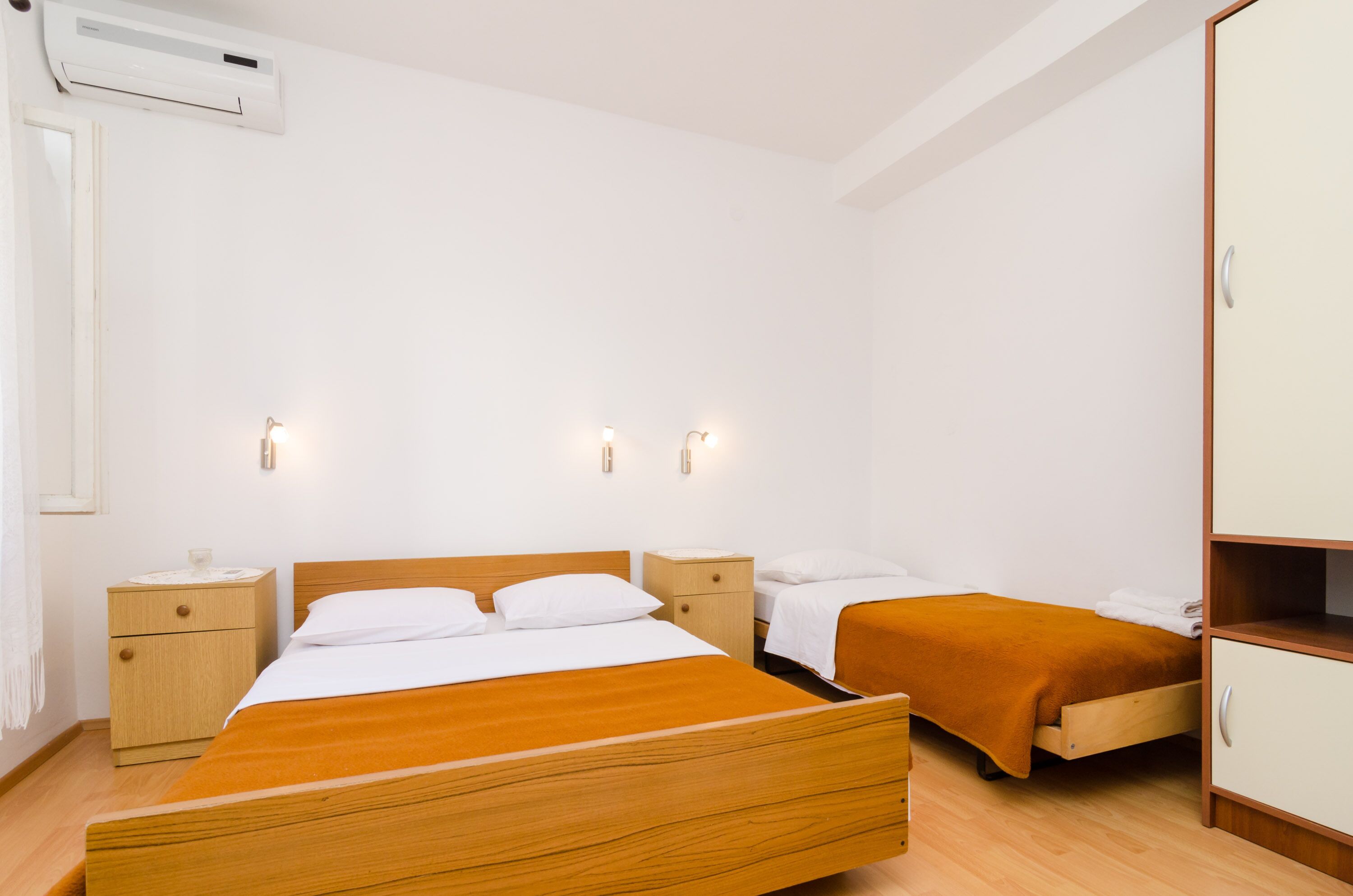 Una habitación con una cama grande, dos mesitas de noche, un armario y un aire acondicionado de pared.