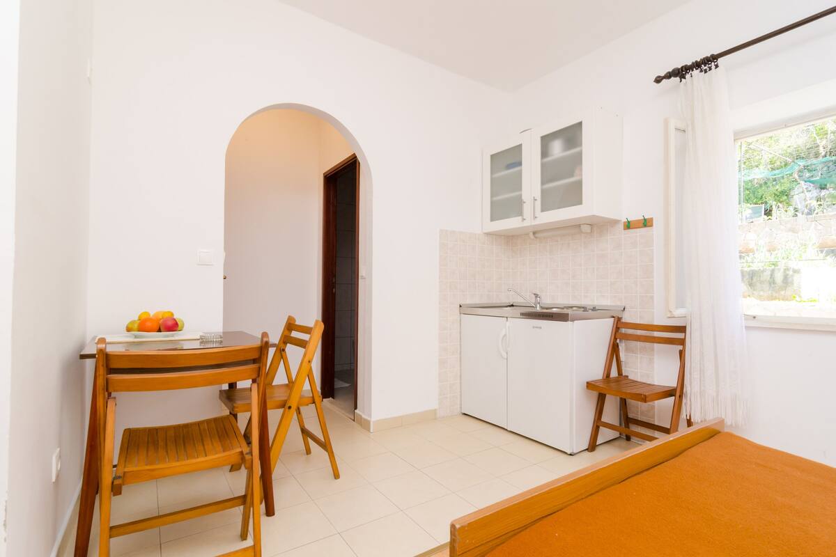 A compact kitchen with white cabinets, a sink, and a window with a view of greenery.