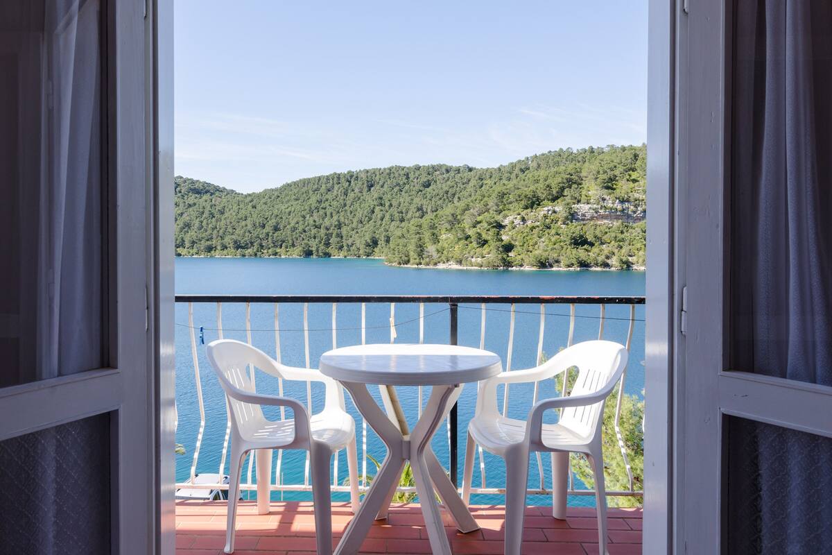 A balcony with a table and two chairs, overlooking a lake and forested hills.
