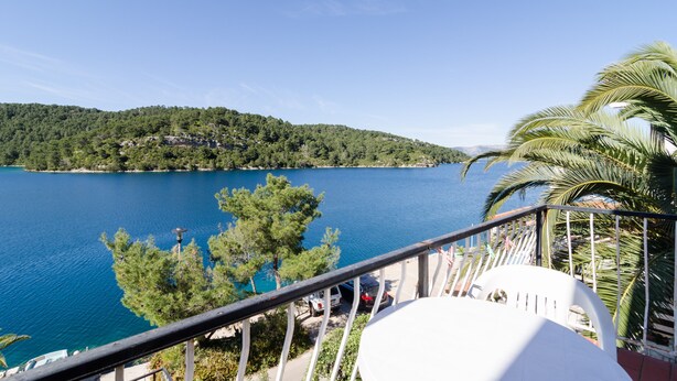 A balcony with a view of a lake and a forested hill. - Apartments Palma (Mljet)