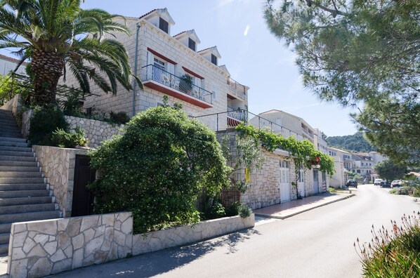 Una calle residencial con edificios de piedra, balcones y abundante vegetación.