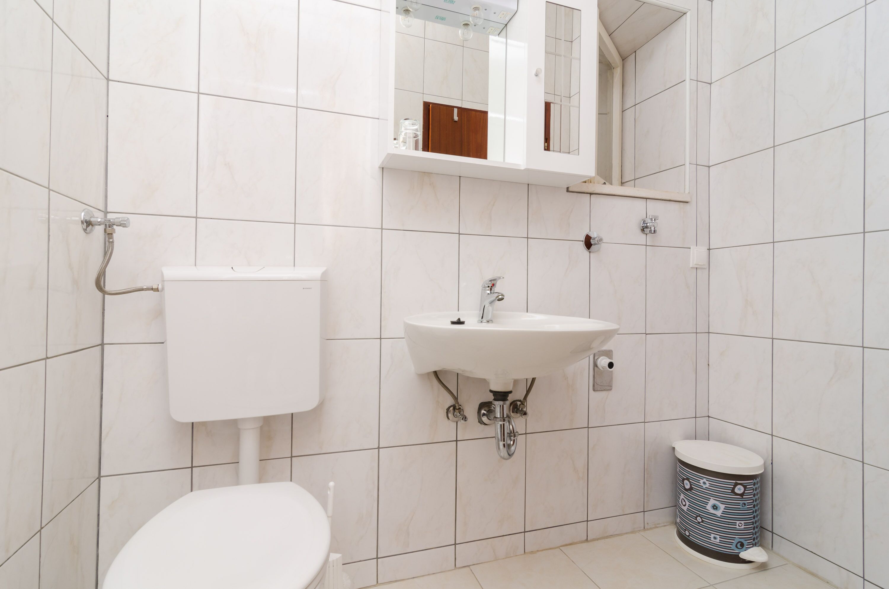 Un bagno con il water, un lavandino, uno specchio e un cestino.