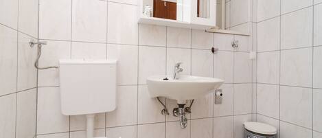 Un bagno con il water, un lavandino, uno specchio e un cestino.