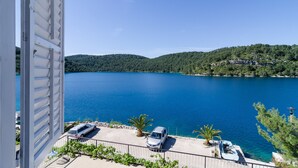 A balcony with a view of a lake, a parked car, and a boat. - Apartments Palma (Mljet)