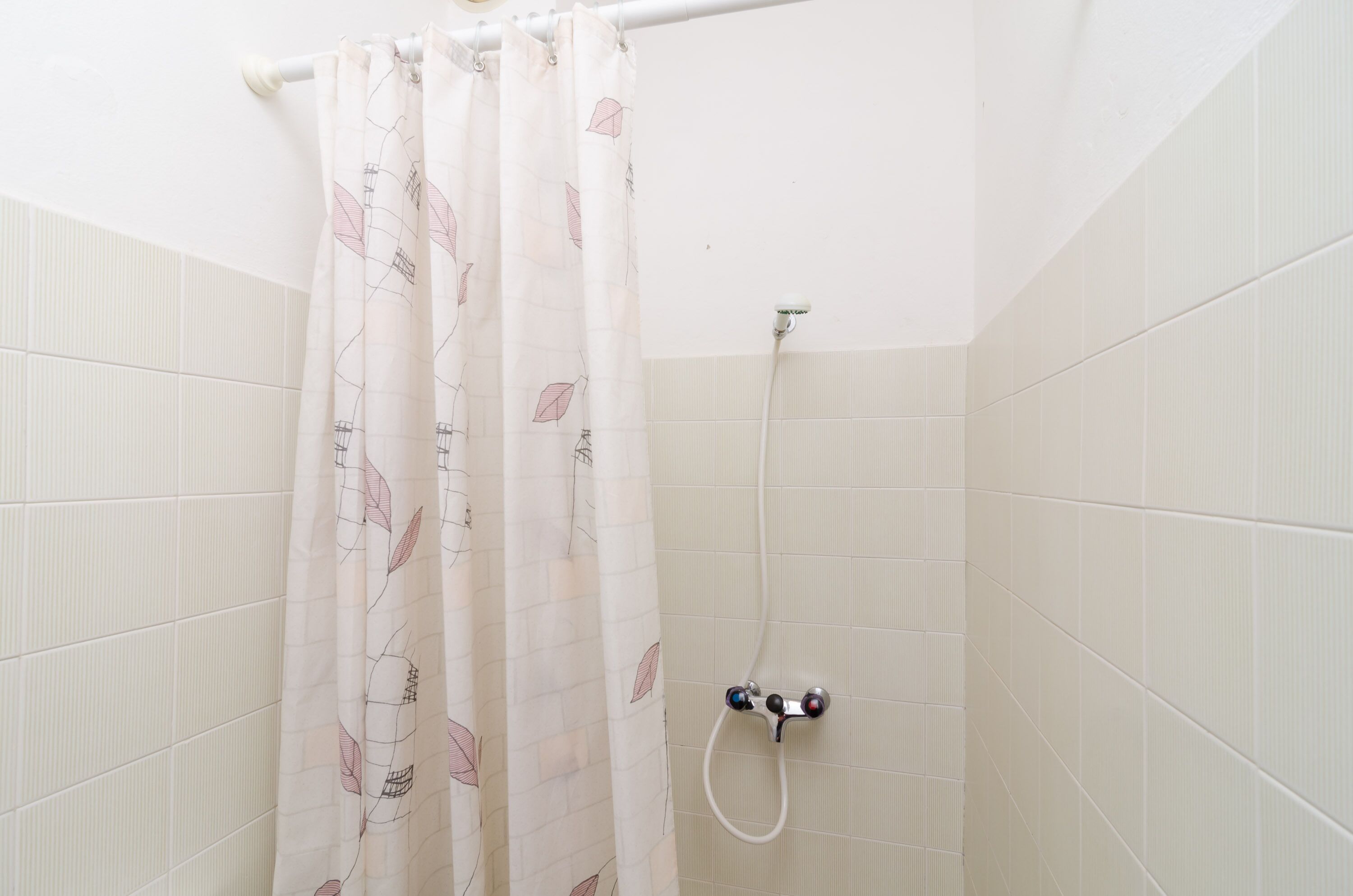 A shower area with a white tiled wall, a showerhead, and a curtain with a leaf pattern.
