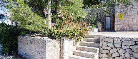 Un escalier en pierre mène à un bâtiment dont le mur est également en pierre et sur lequel est apposée une enseigne indiquant un numéro.