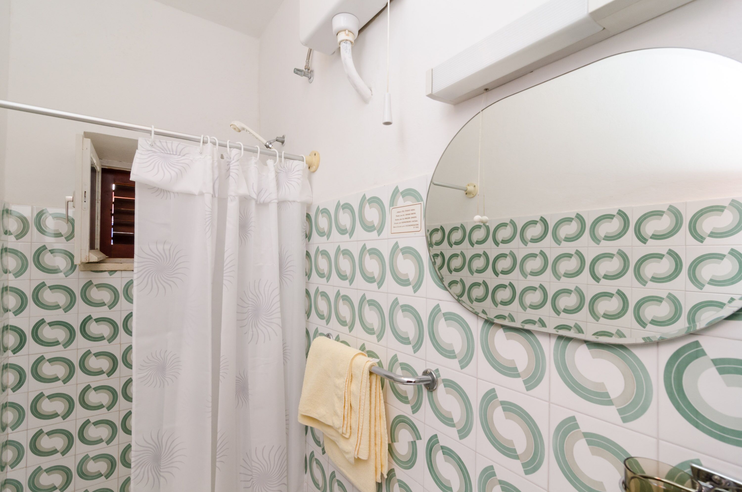 A bathroom with a shower curtain, a towel rack, a mirror, and patterned tiles.