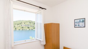 A bedroom with a wooden headboard, a window with white curtains, and a framed picture on the wall. - Apartments Palma (Mljet)