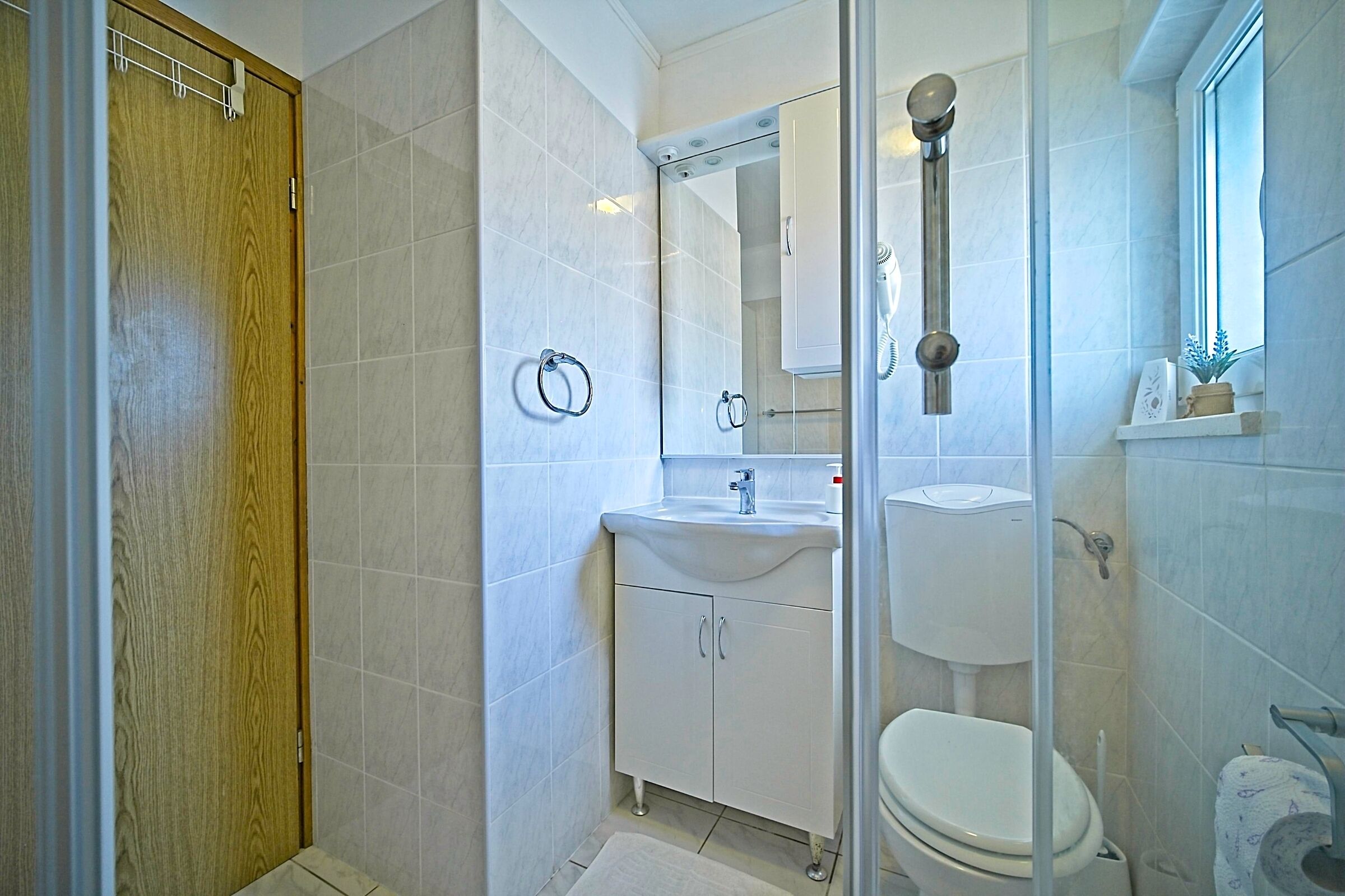 Ein modernes Badezimmer mit Holztür, weißen Fliesen und einer Dusche, inklusive Waschbecken und Toilette.