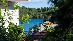 A coastal view with a clear blue sea, a stone building with a red roof, and lush greenery. - Guest House Matana Pomena (Mljet)
