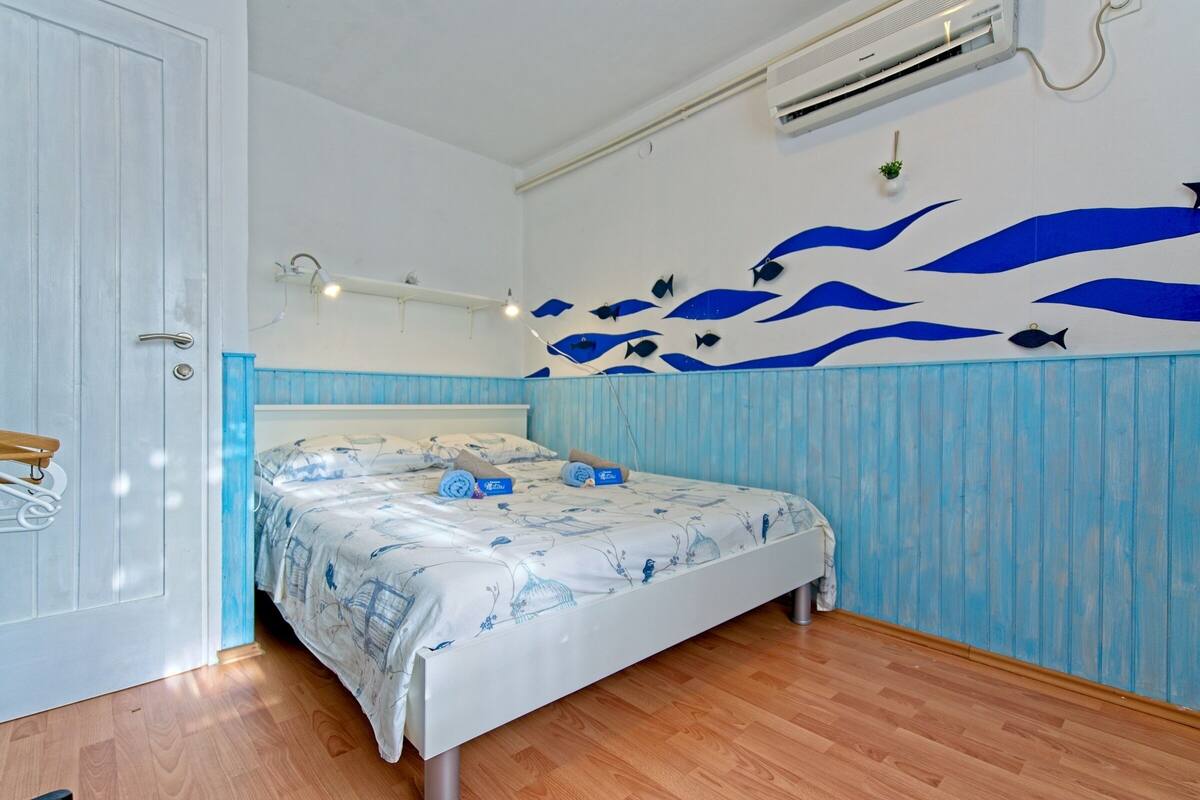 A bedroom with a bed, a wooden floor, a white door, and a wall with blue wave patterns.