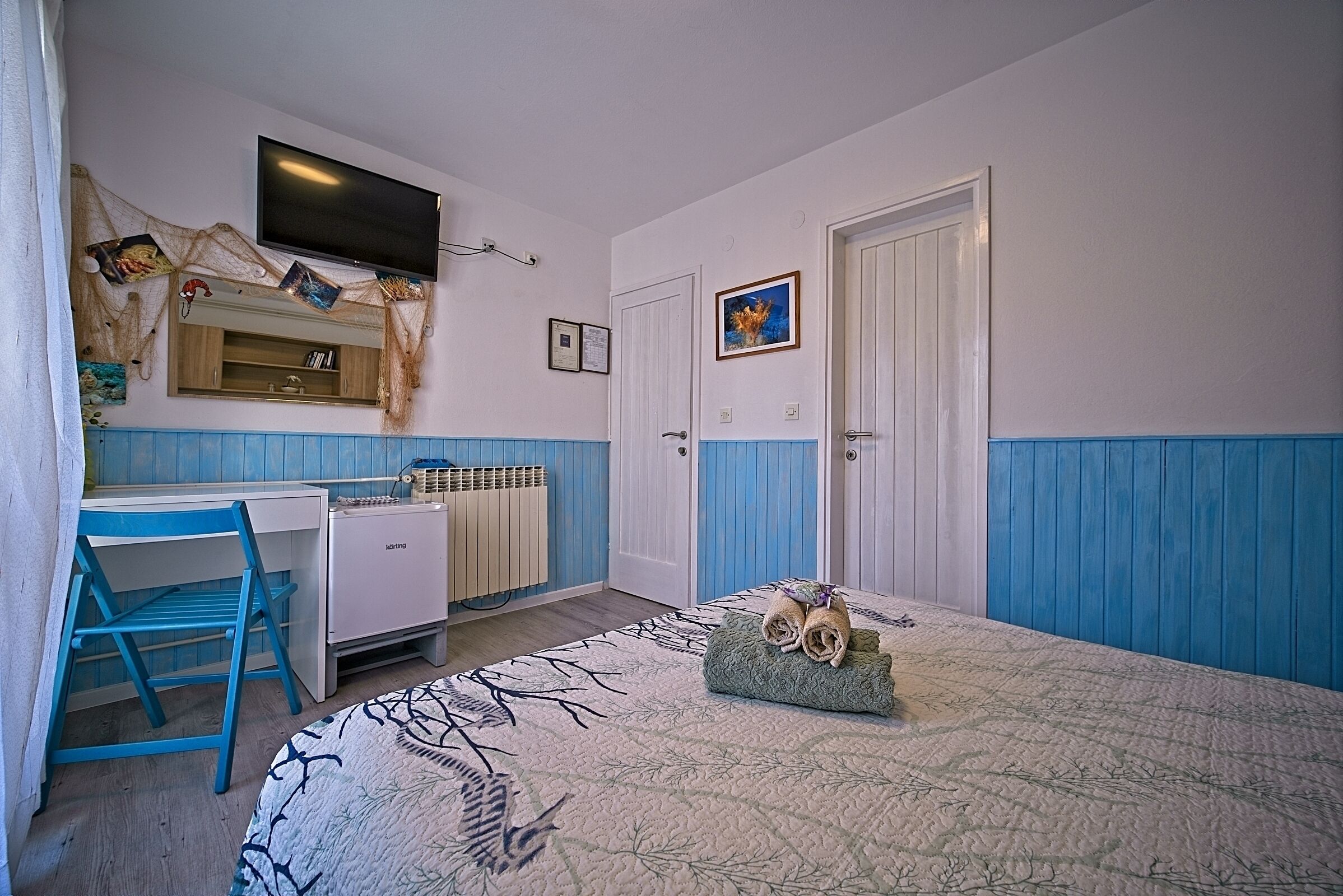 Una habitación con cama, escritorio, silla, televisor y radiador.