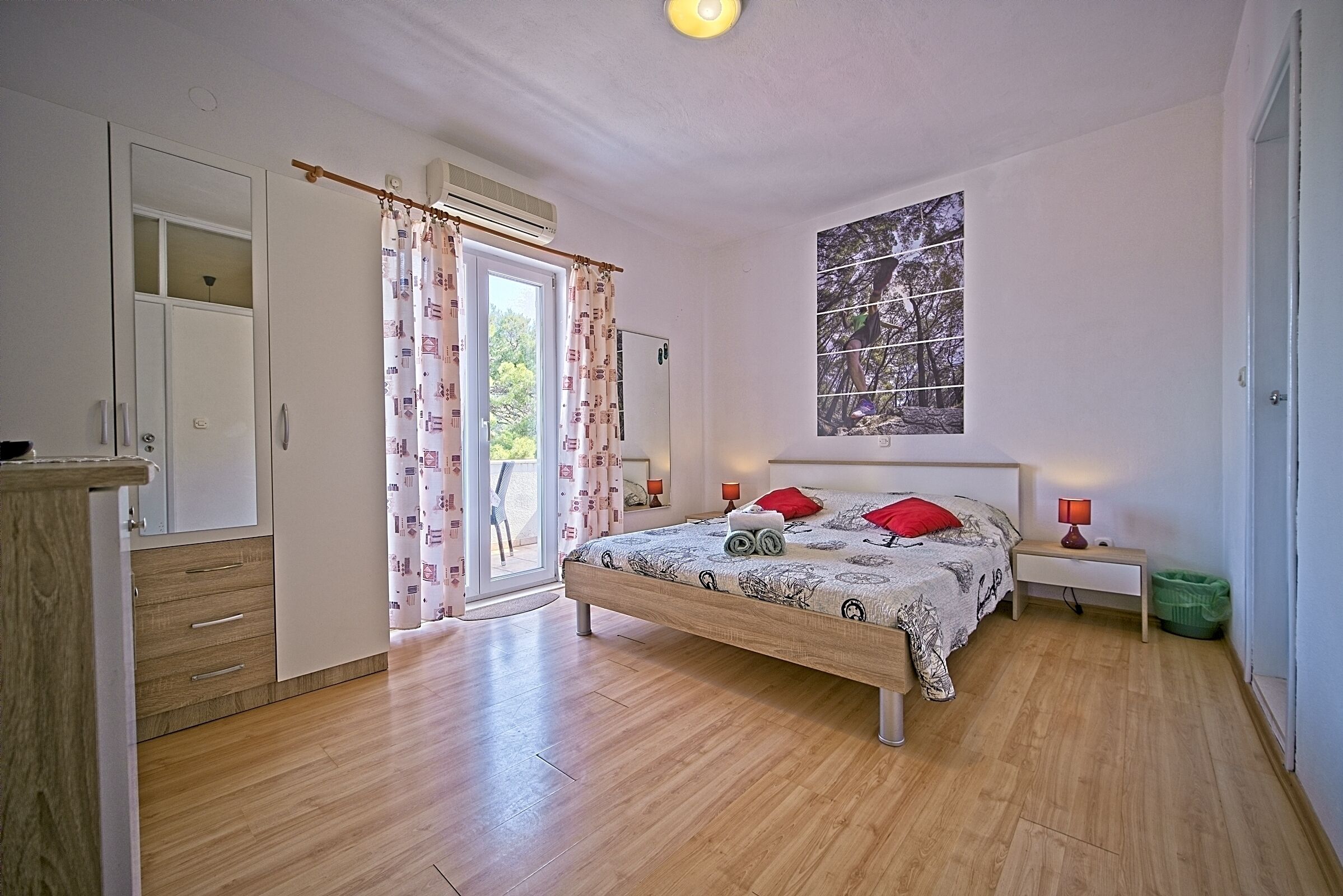 A bedroom with a bed, a nightstand, a window with a view, and a door.