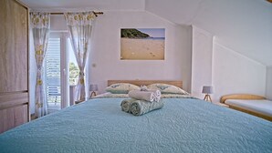 A bedroom with a large bed, a painting of a beach, and a view of the outdoors. - Guest House Matana Pomena (Mljet)