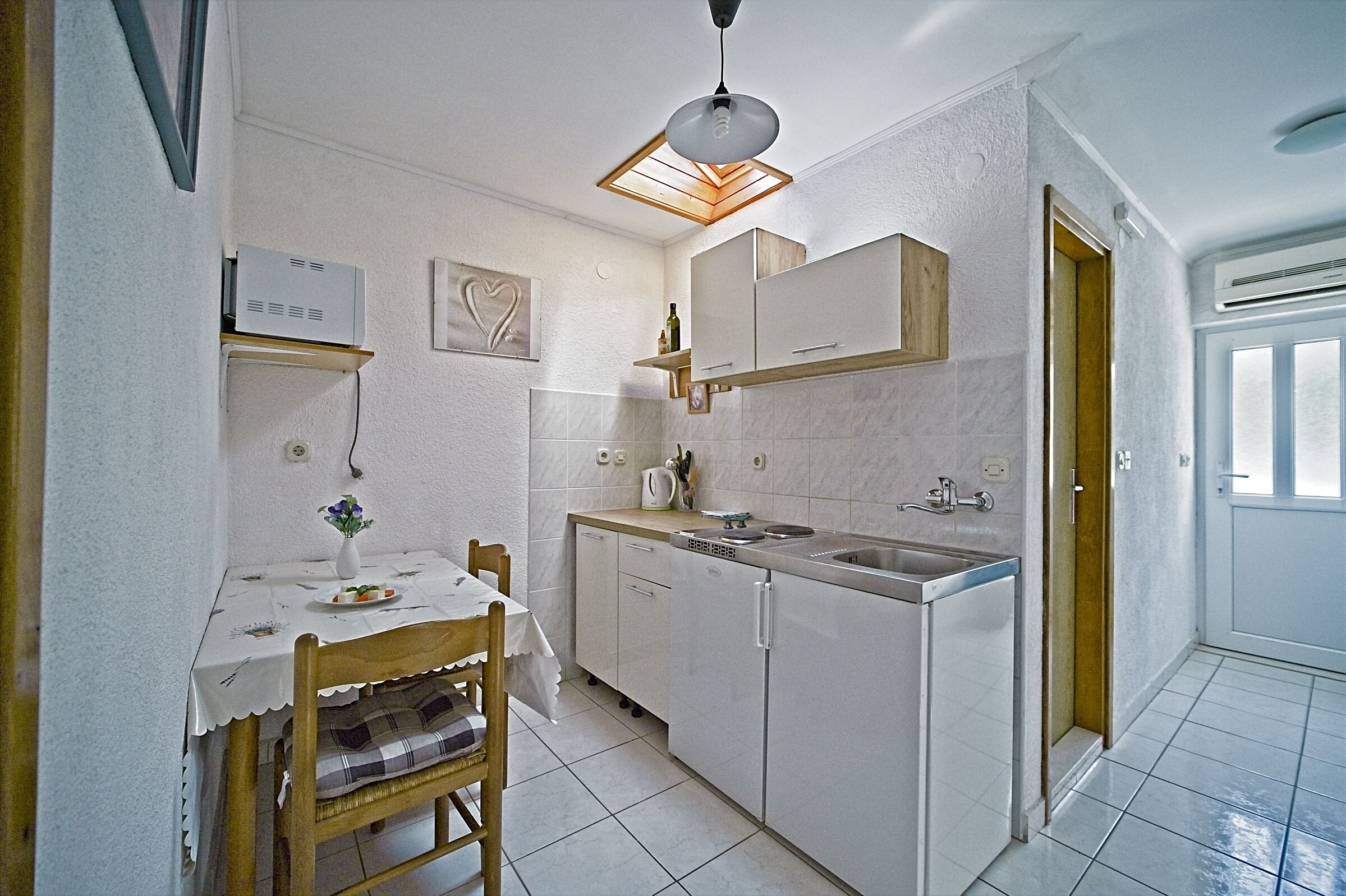 A compact kitchen with white cabinets, a dining table with a chair, and a pendant light.