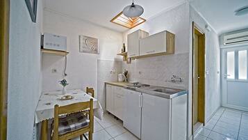 A compact kitchen with white cabinets, a dining table with a chair, and a pendant light.