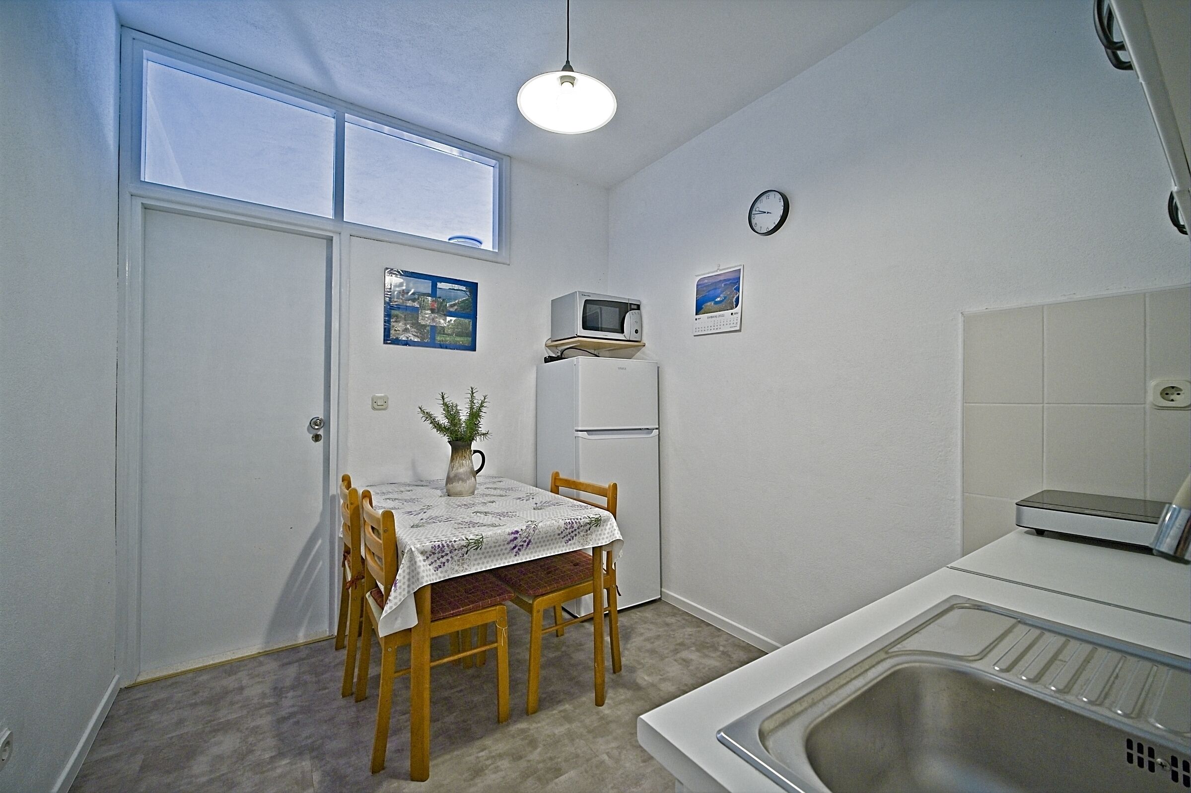 A compact kitchen with a dining table, chairs, a microwave, a refrigerator, and a sink.