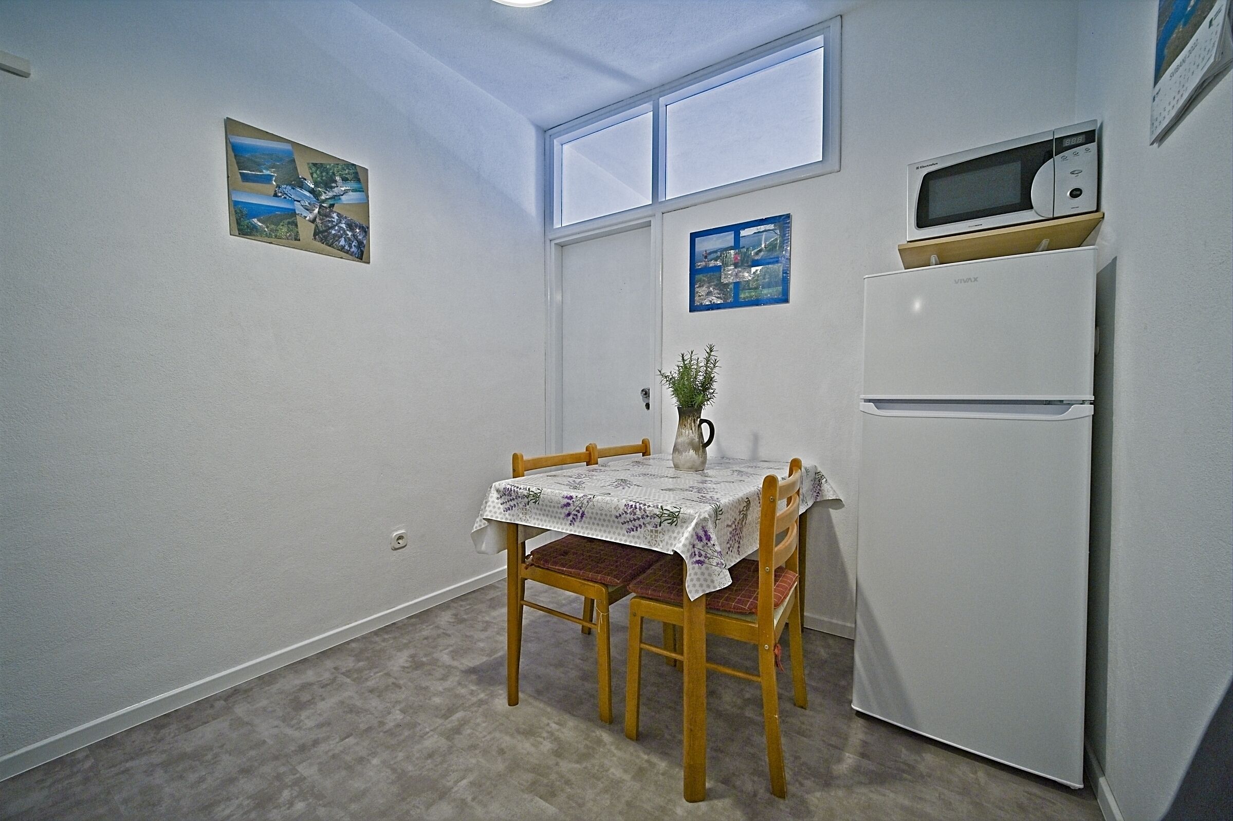 A small kitchen with a dining table, chairs, a refrigerator, and a microwave on top.