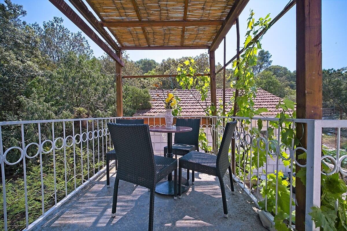 A covered outdoor seating area with wicker chairs and a table, surrounded by a metal fence and greenery.