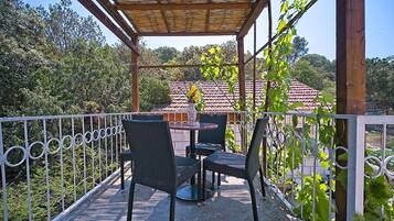 Un espace extérieur abrité, aménagé avec des chaises en osier et une table, entouré d’une clôture en métal et de verdure.