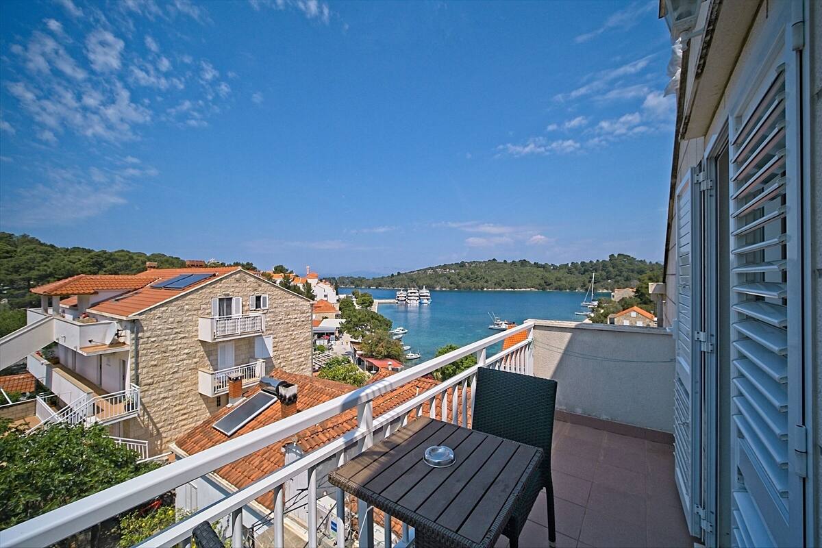 A balcony with a table and chairs overlooking a coastal area with buildings and boats.