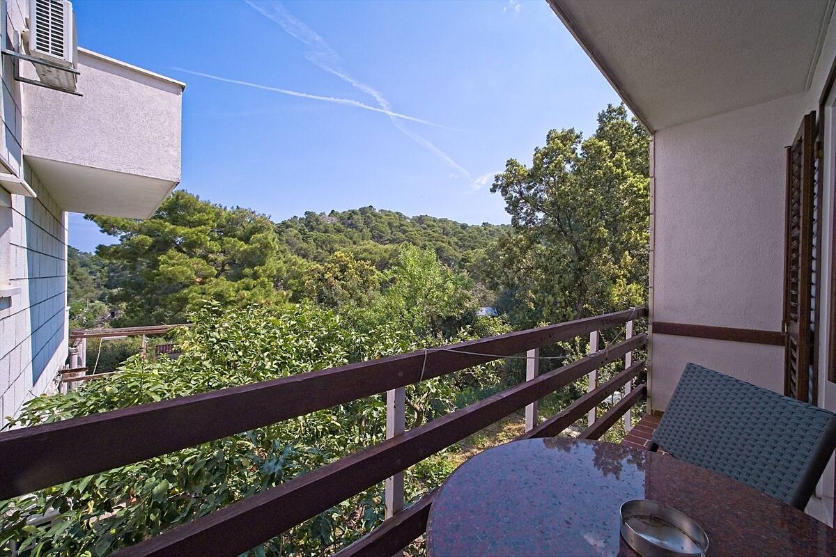 A balcony with a table and chair, overlooking a lush green hillside.