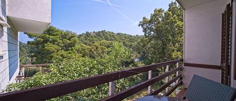 A balcony with a table and chair, overlooking a lush green hillside.