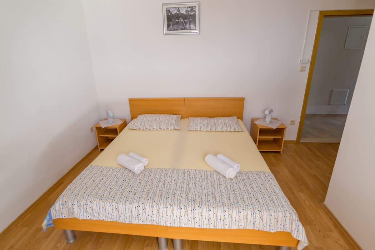 Cama doble con colcha estampada, dos almohadas y dos mesitas de noche con lámparas.