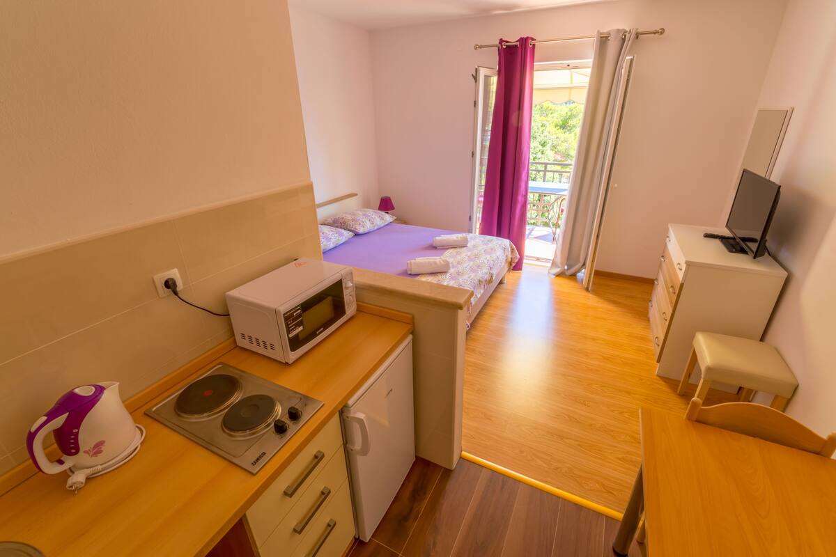 Una habitación de hotel compacta con kitchenette, una cama, un escritorio pequeño y un televisor.