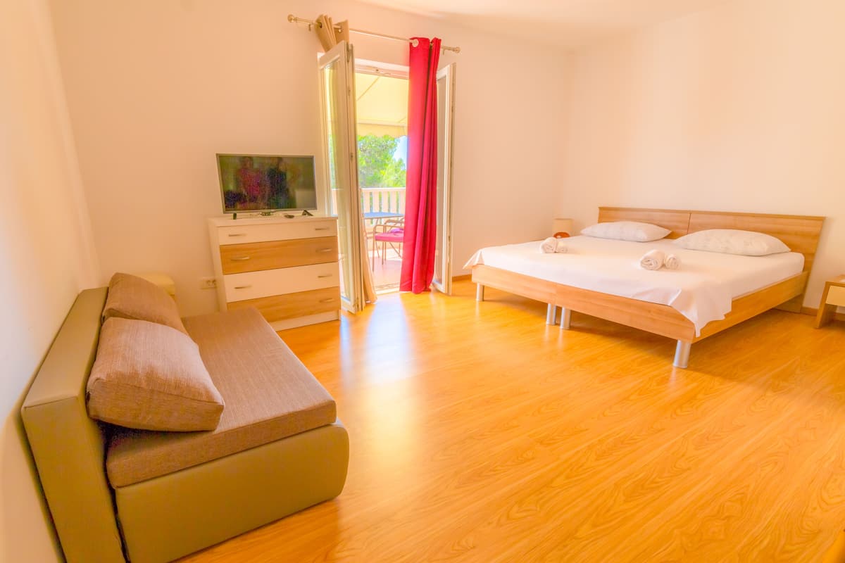 Un dormitorio con cama, sofá, televisor en una cómoda y balcón con cortinas rojas.