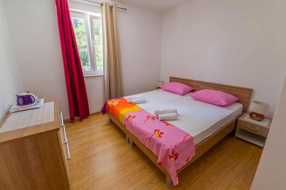 Un dormitorio ordenado con cama, mesita de noche y escritorio con hervidor.