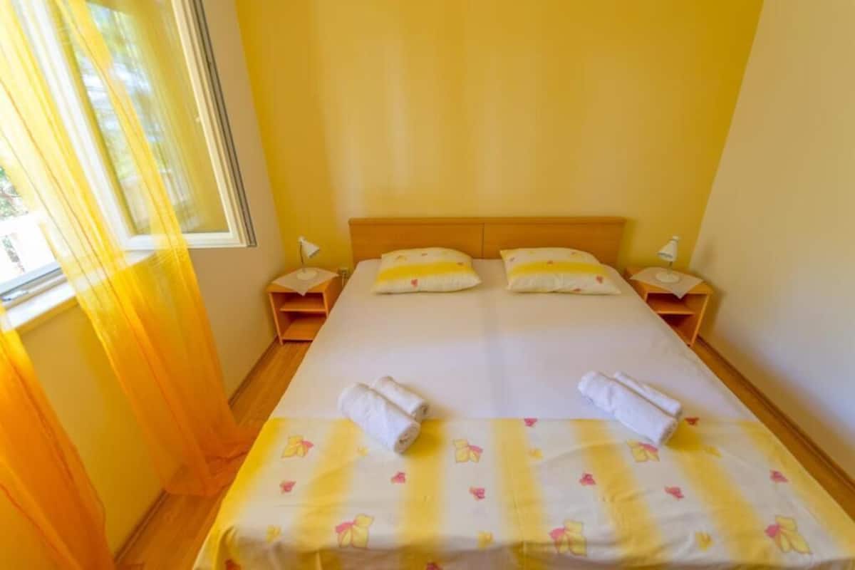 Una habitación de hotel con una cama, dos mesitas de noche y una ventana con cortinas.