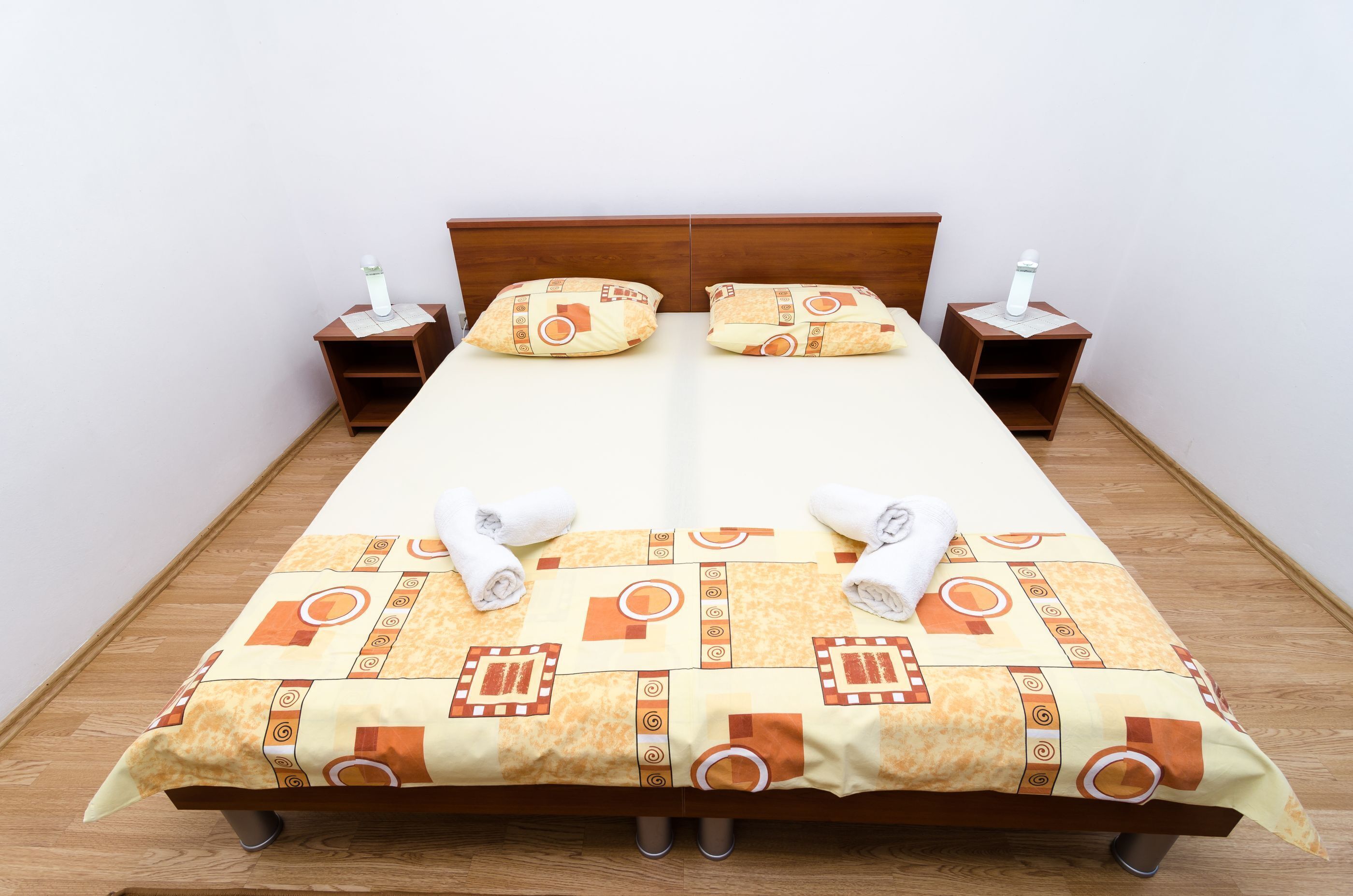 A neatly made bed with a patterned bedspread, two pillows, and two bedside tables with lamps.