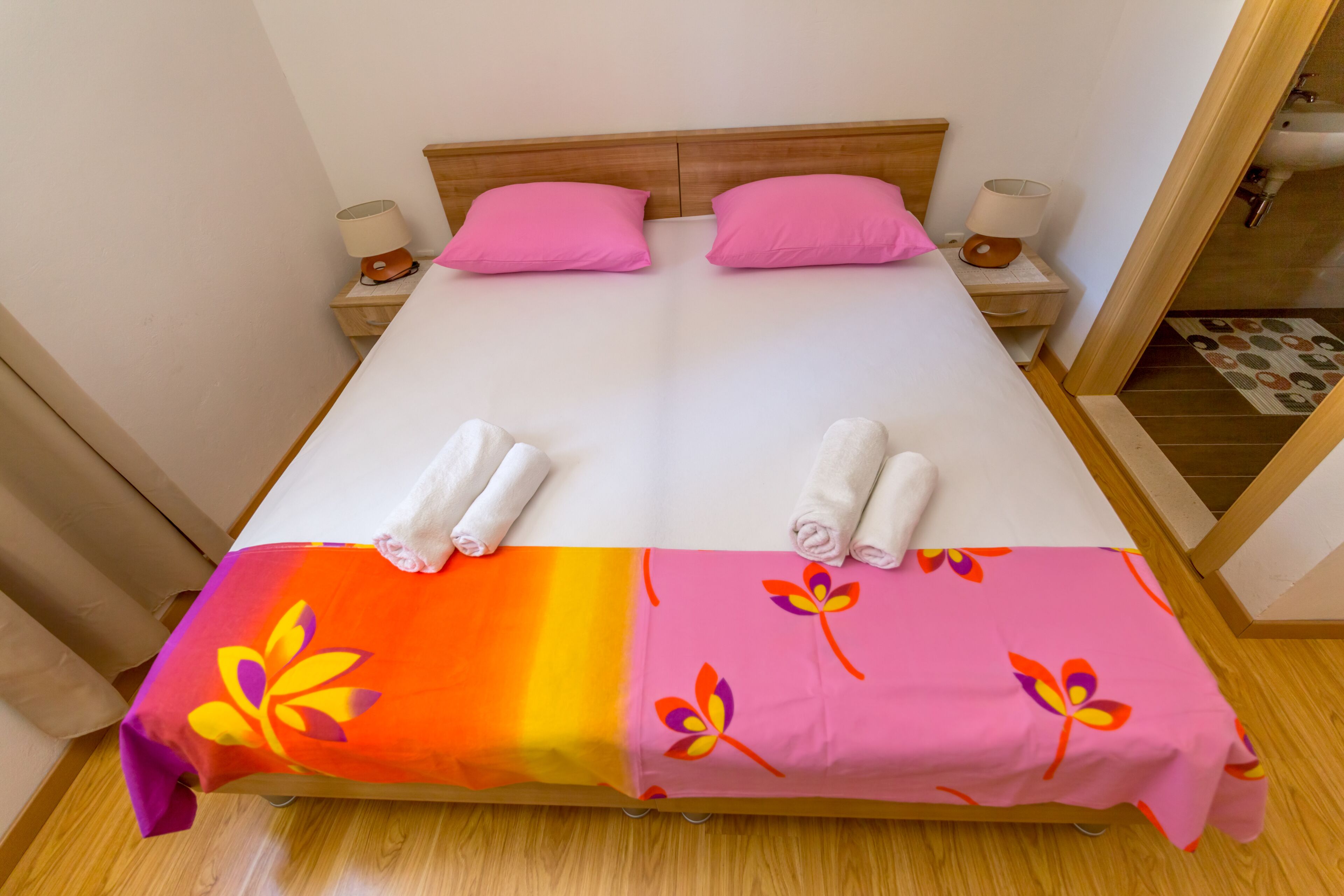 A double bed with pink pillows, a wooden headboard, and a bedside table with a lamp.