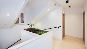 Ein modernes Interieur mit schrägverdeckter Decke, einem kleinen Fenster und einem Pflanzgefäß mit Pflanzen.