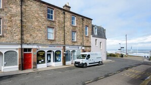 A street view with a row of buildings, including a computer shop and a physiotherapy center. A white van is parked on the side of the road. - Cosy Rest (North Berwick)