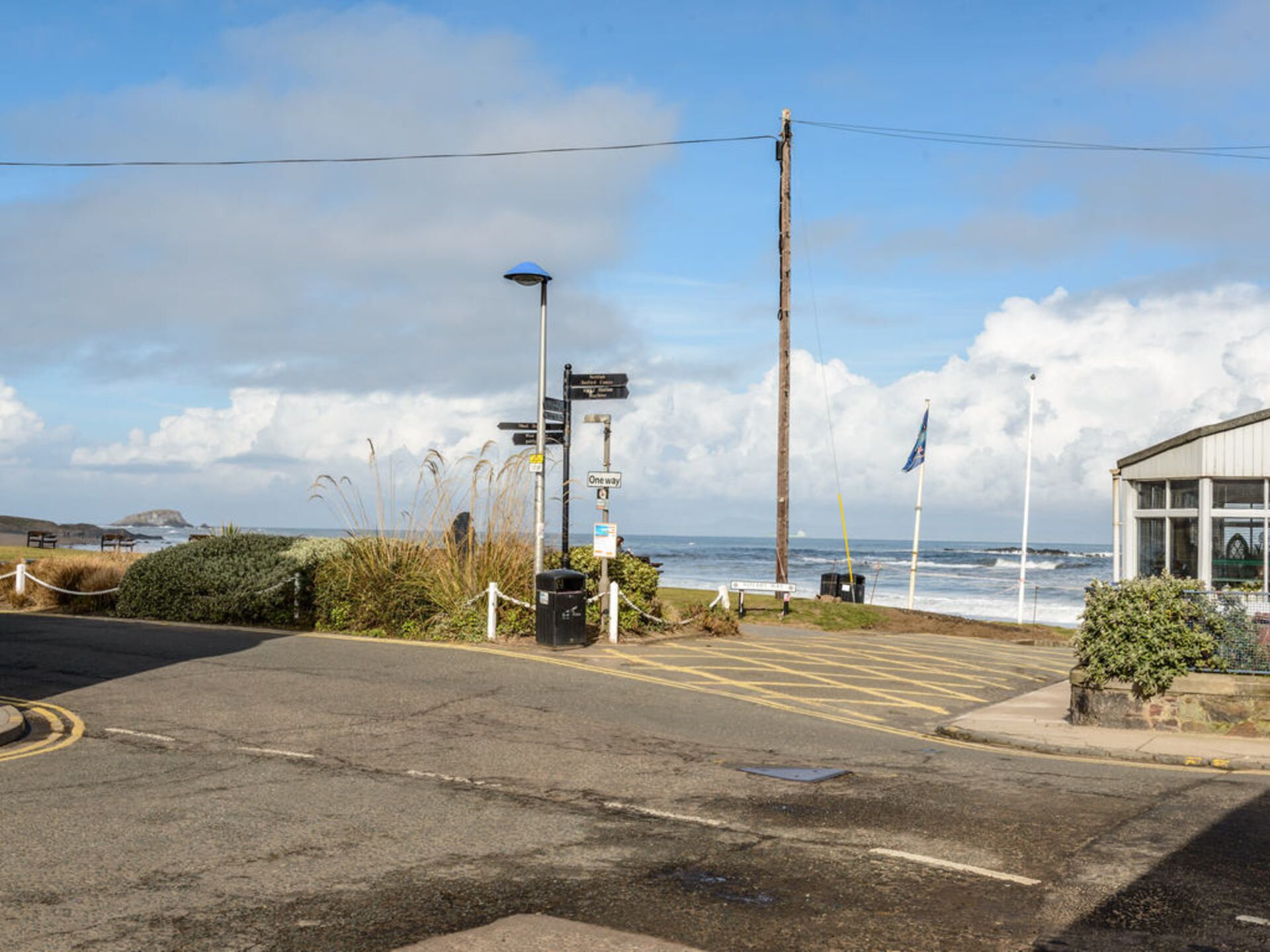 A coastal road with directional signs, a beach, and a building with large windows overlooking the sea.