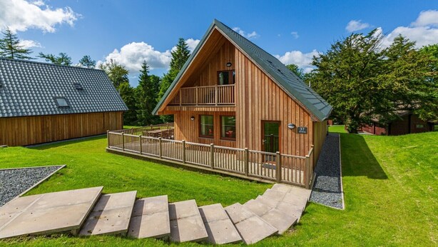 Een houten chalet met balkon, overdekte veranda en een nummerbord dat de locatie aangeeft.
