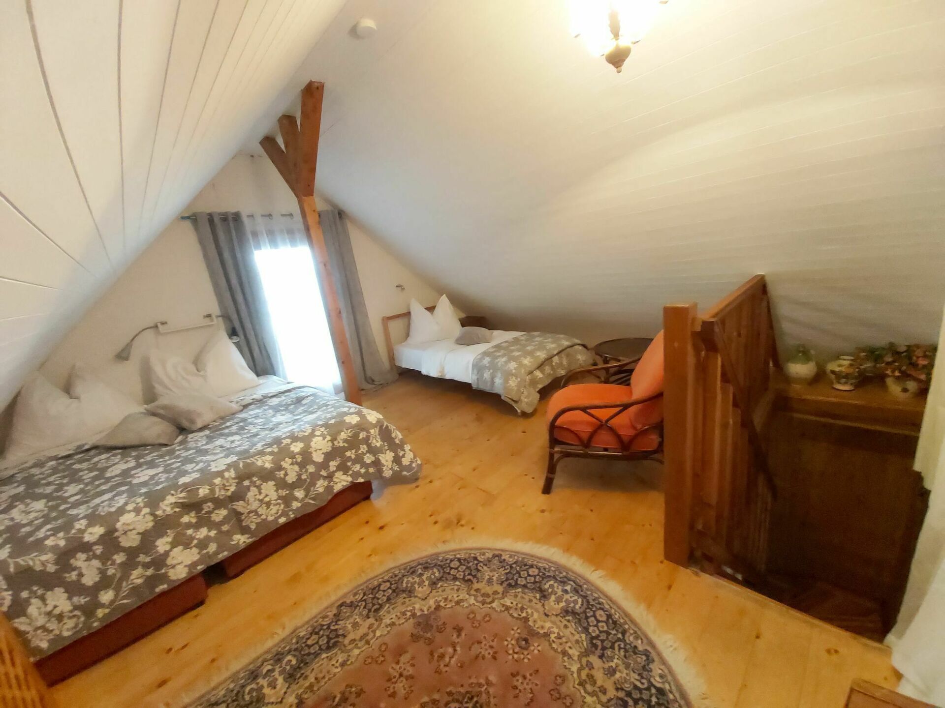 Un dormitorio acogedor en el ático con dos camas, una silla, una mesita y una alfombra.