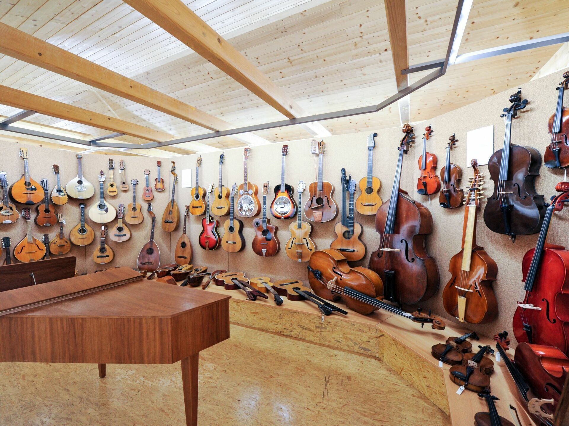 Una stanza con soffitto e pareti in legno, dove sono esposti vari strumenti a corda come chitarre, violini e violoncelli.