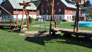 A playground with swings and a slide, surrounded by houses and a swimming pool.