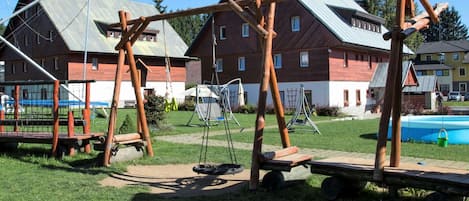 A playground with swings and a slide, surrounded by houses and a swimming pool.