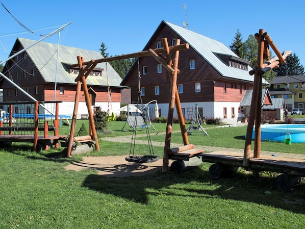 A playground with swings and a slide, surrounded by houses and a swimming pool.
