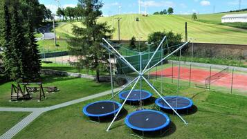 A playground with multiple trampolines, a tennis court, and wind turbines in the background.