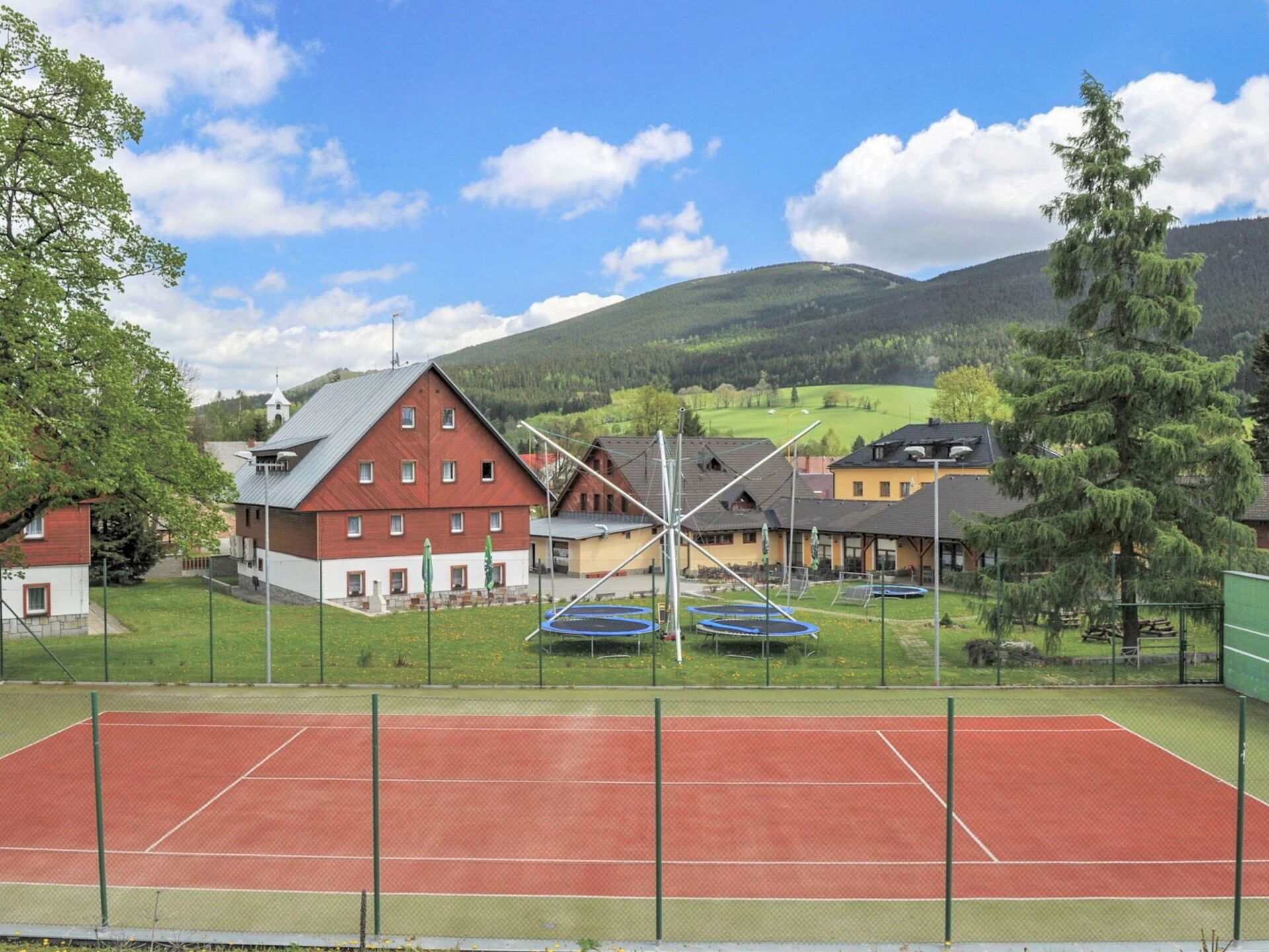 Una cancha de tenis con una red, rodeada por una cerca, y edificios al fondo.